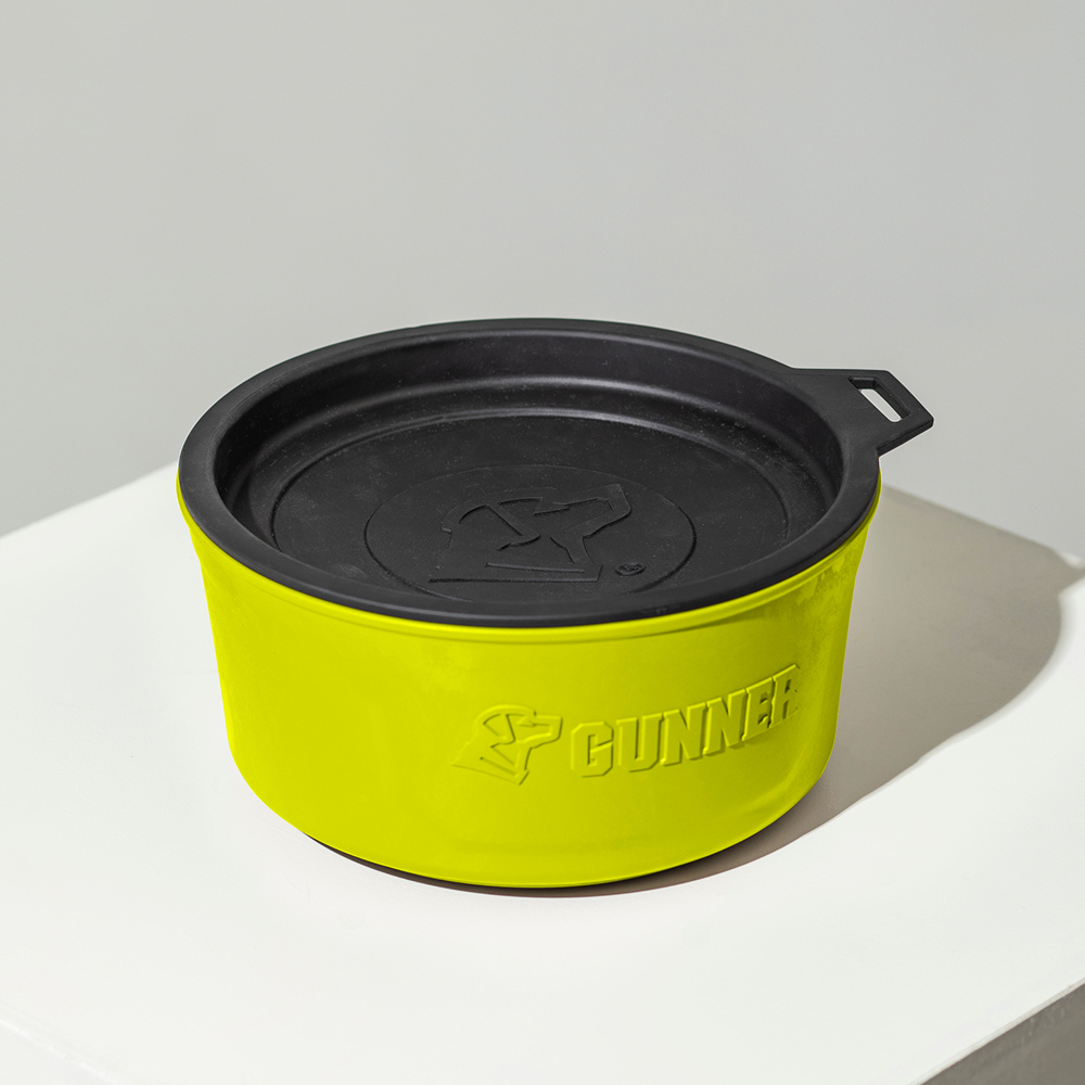 A bright yellow GUNNER DOG BOWL - SULPHUR SPRINGS from GUNNER, featuring a black lid and an embossed dog logo and brand name, sits on a white surface.
