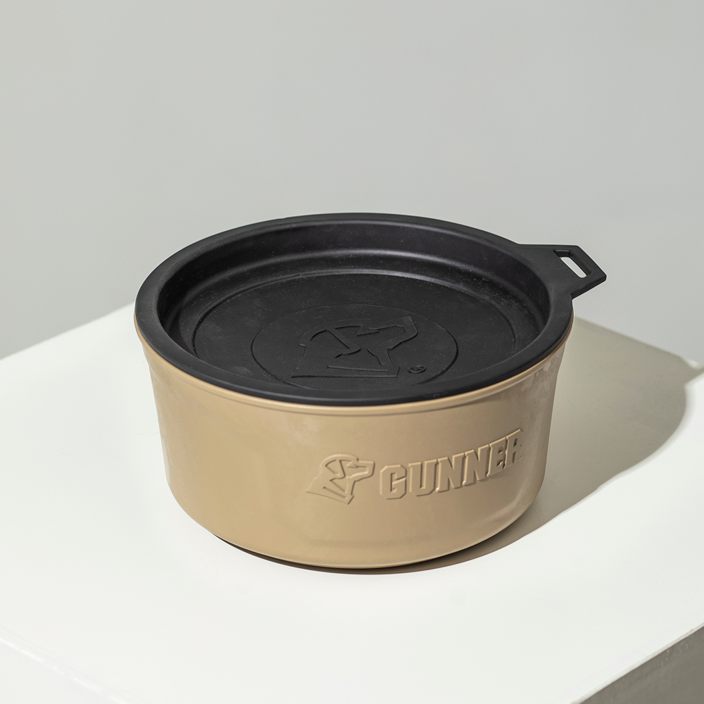 The GUNNER DOG BOWL - TAN by GUNNER is a beige, round dog bowl with a black lid and an embossed GUNNER logo, shown on a white surface against a plain background.