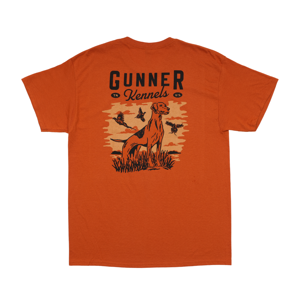 The GUNNER UPLAND TEE is an orange shirt featuring GUNNER text above a graphic of a dog on point in grass, watching ducks fly across a sunset backdrop.