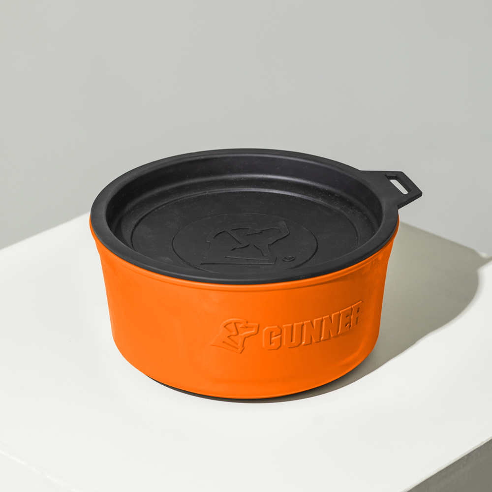 The GUNNER DOG BOWL - BLAZE ORANGE, a round orange and black container with lid and embossed GUNNER logo, from the limited-edition Color Fetch collection, is shown on a white surface with a light gray background.