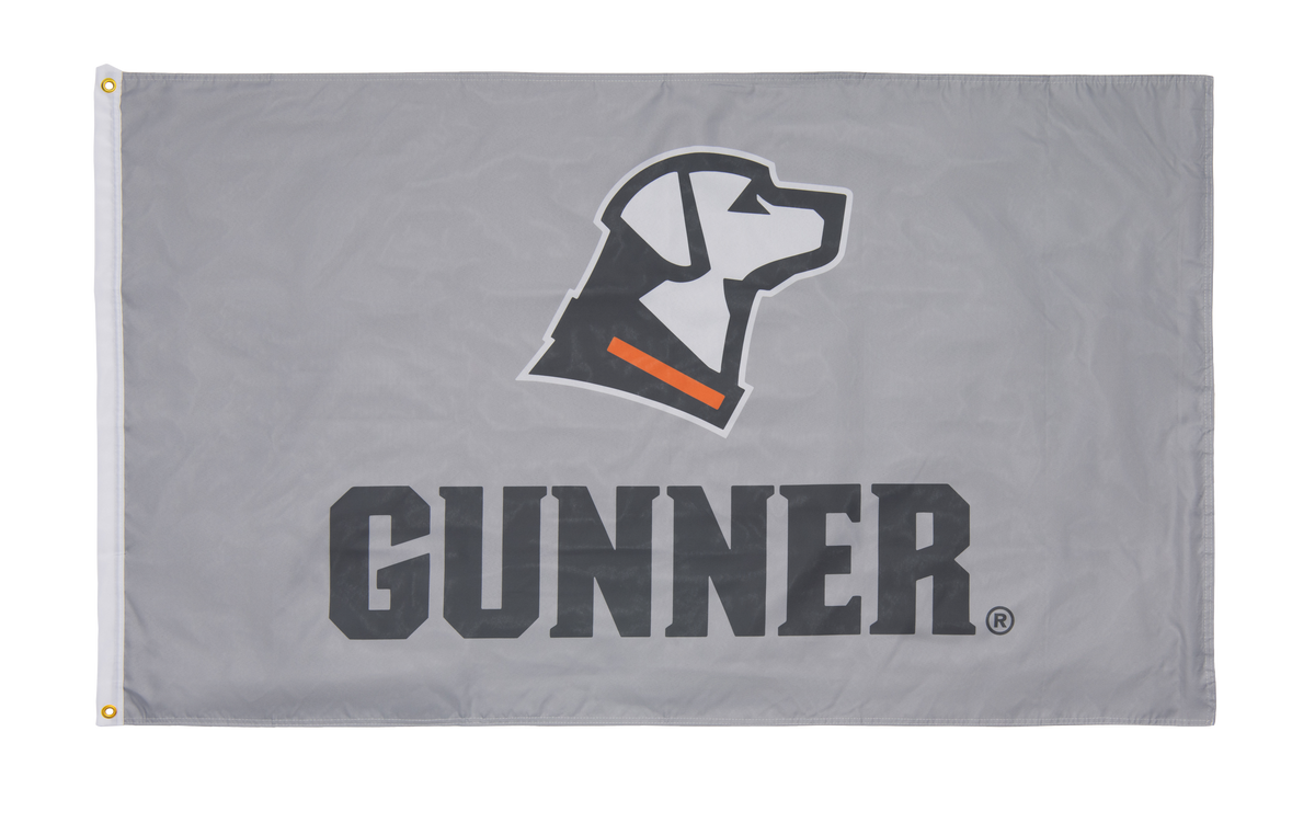 The GUNNER FLAG is a lightweight flag featuring a black and white dog head logo with an orange collar above bold black GUNNER text—ideal for shop décor or displaying your GUNNER pride.