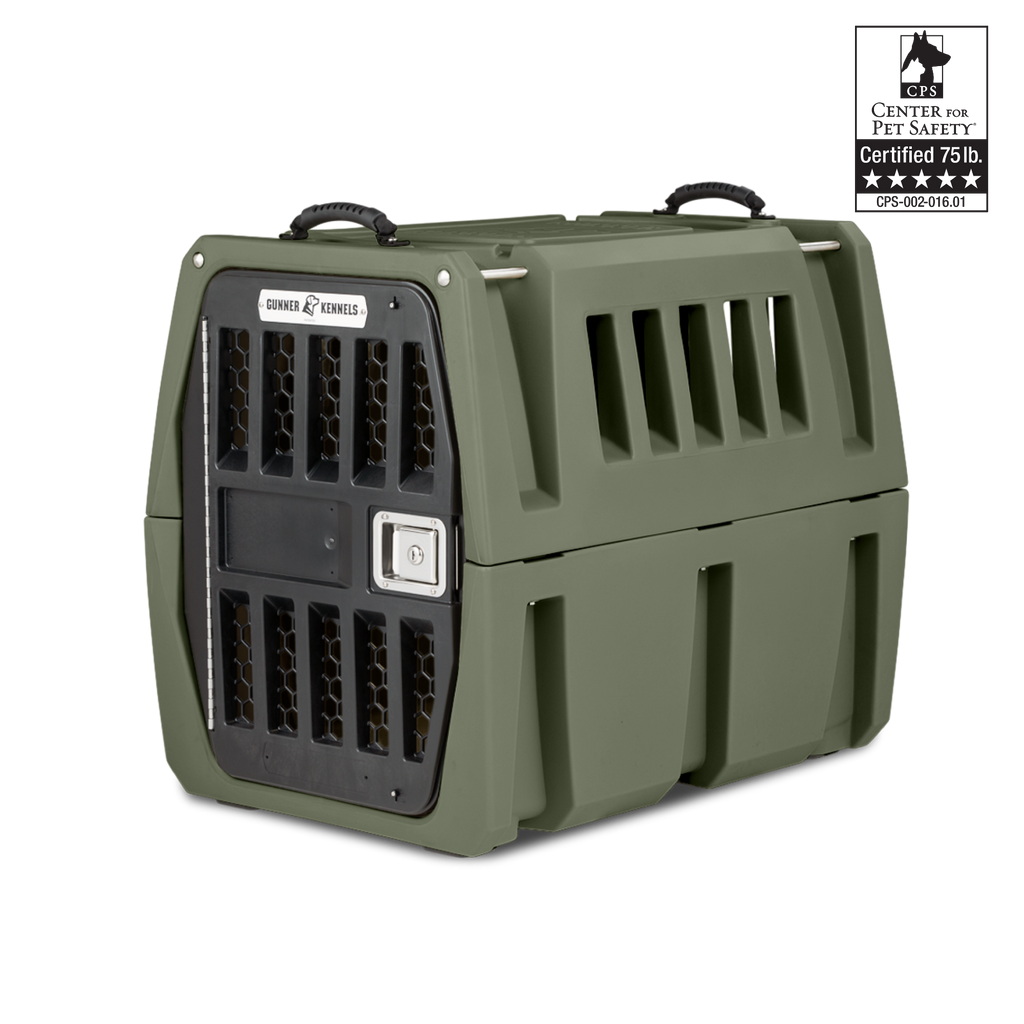 A sturdy olive-green dog kennel with ventilation slats and a black, secure metal door. The top features carry handles—ideal outdoor gear for your working dog. A certification badge in the top right reads Center for Pet Safety, Certified 75 lb.