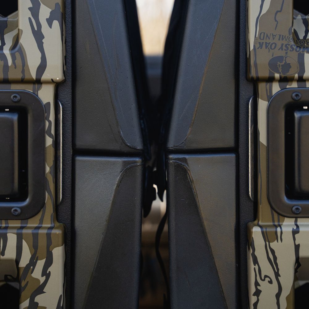Close-up of two camo-patterned vehicle doors with black trim, ideal for transporting the GUNNER G1™ KENNEL - MOSSY OAK BOTTOMLAND BLACK. The narrow gap between the doors forms a vertical line in the center of the image.