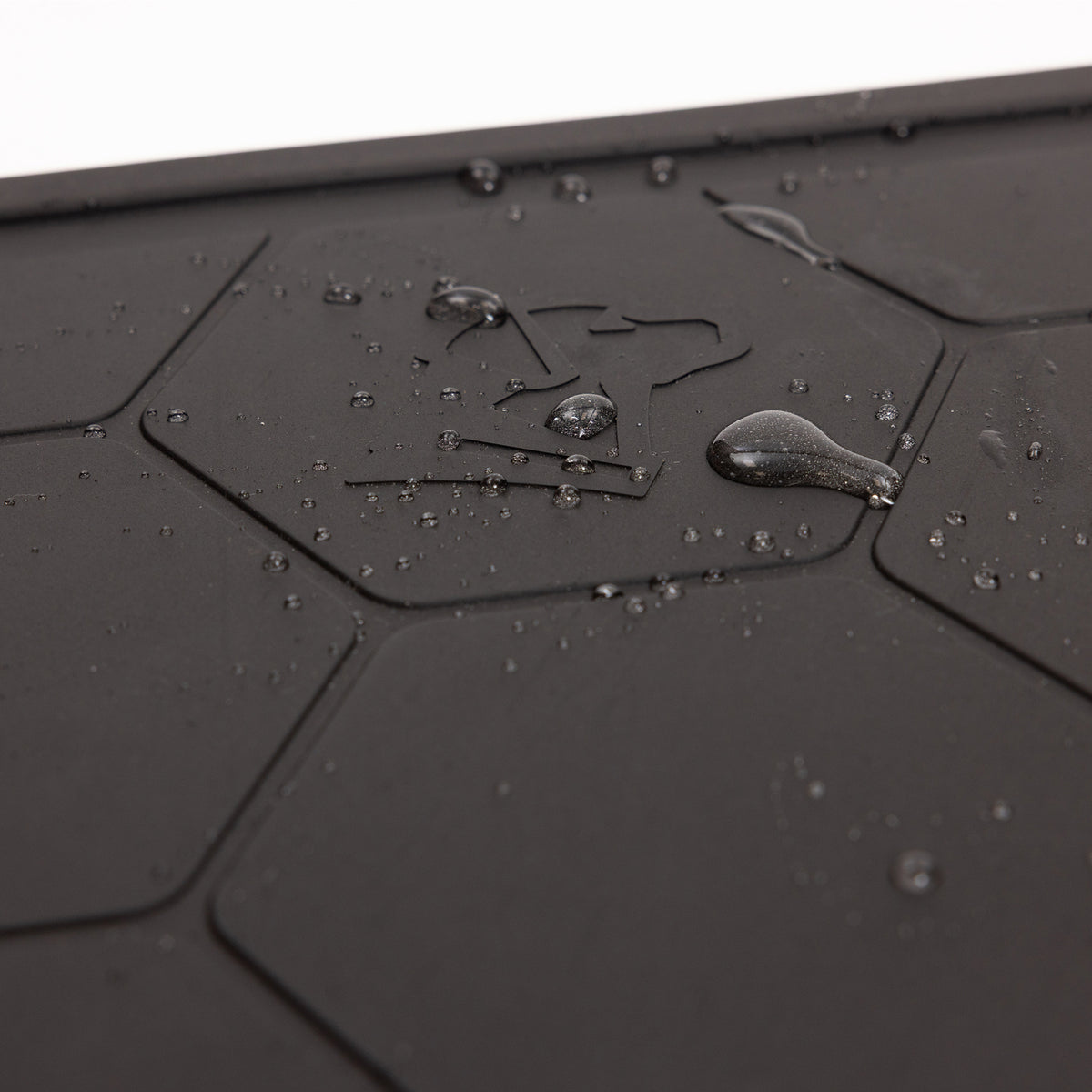 Close-up of water droplets on the GUNNER BOWL MAT - BLACK, featuring hexagonal patterns and an umbrella symbol that indicates its slip-resistant and water-resistant properties.