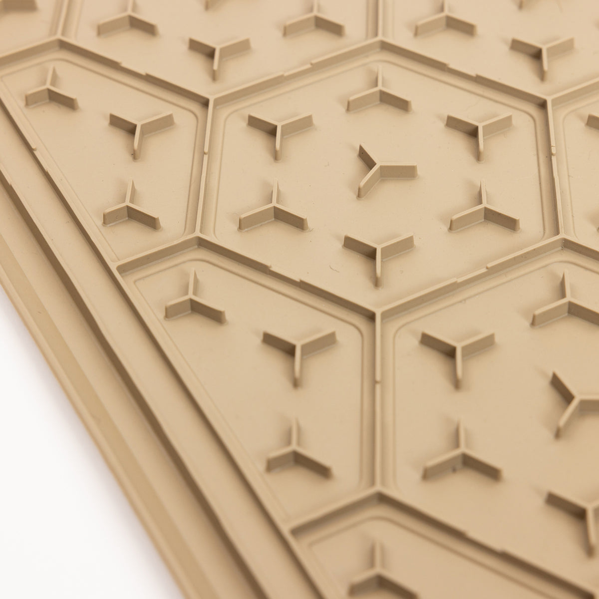 A close-up of the GUNNER BOWL MAT - TAN shows its textured surface featuring hexagonal patterns with small, three-pronged raised shapes inside each hexagon, all designed to be slip-resistant and dishwasher-safe.