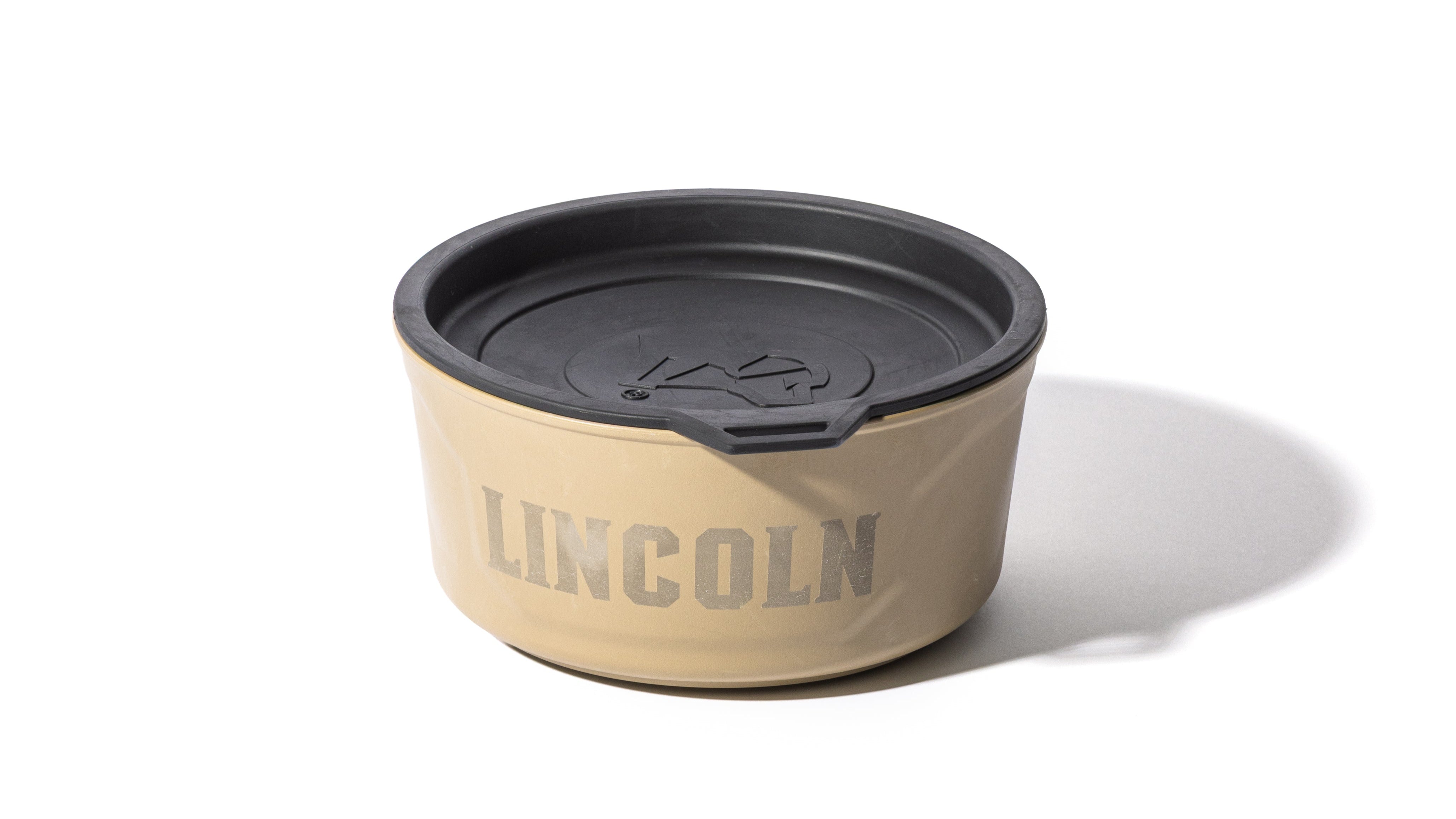 A tan container with the word LINCOLN printed on the side in gray letters, featuring a black plastic lid with a small tab and an embossed mountain design—perfect for storing outdoor gear for your next hunting dog adventure.