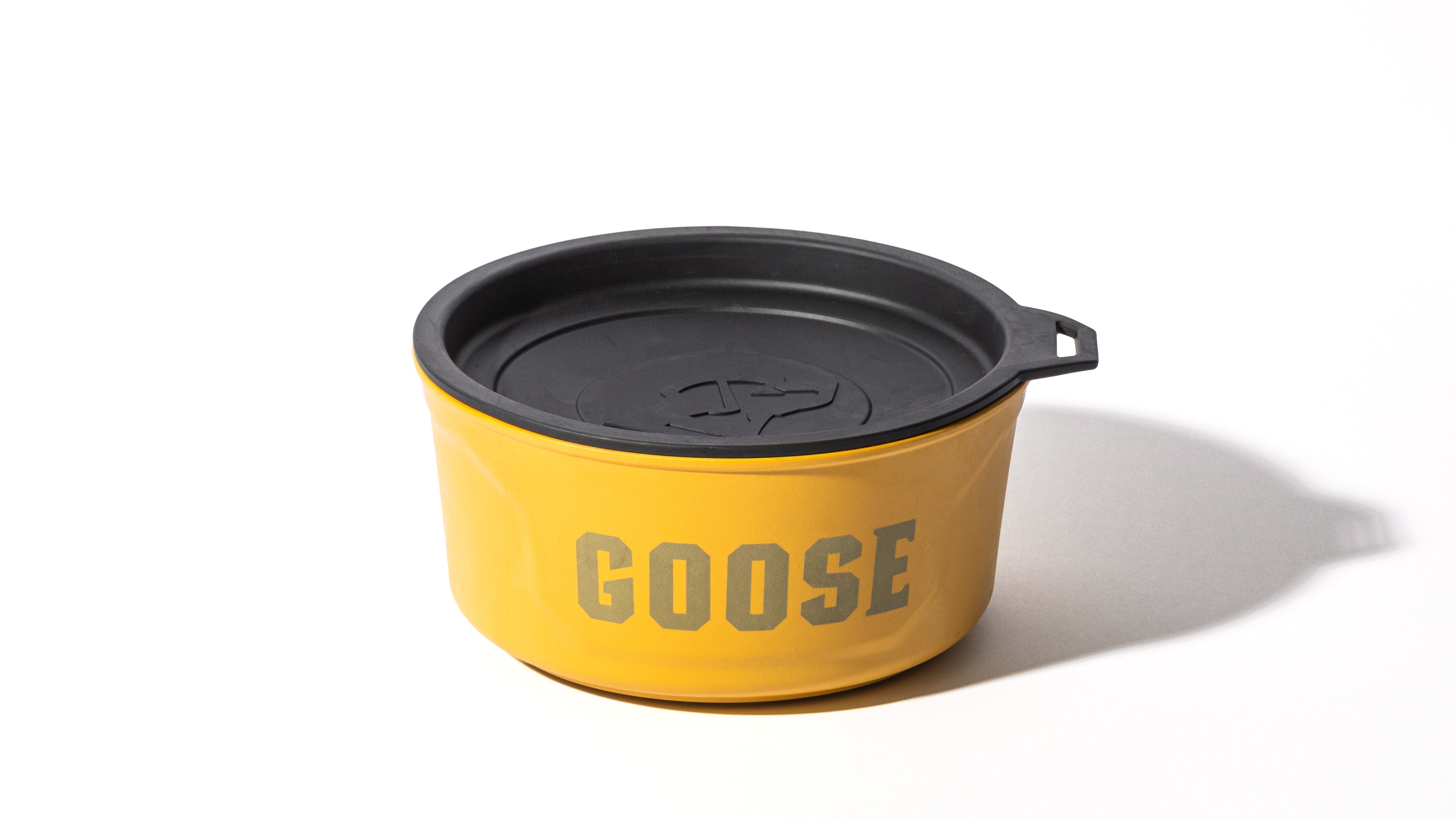 A yellow container with a black lid, featuring the word GOOSE printed in bold gray letters on the side, resembles a stylish dog crate. The container casts a shadow on a white background.