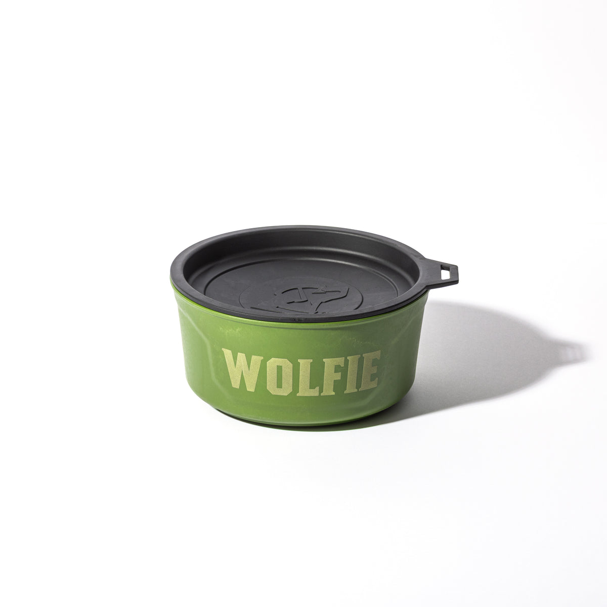 A GUNNER DOG BOWL - DUCK GREEN by GUNNER, featuring a black lid and “WOLFIE” in bold yellow letters on the front, sits on a white surface and casts a soft shadow.