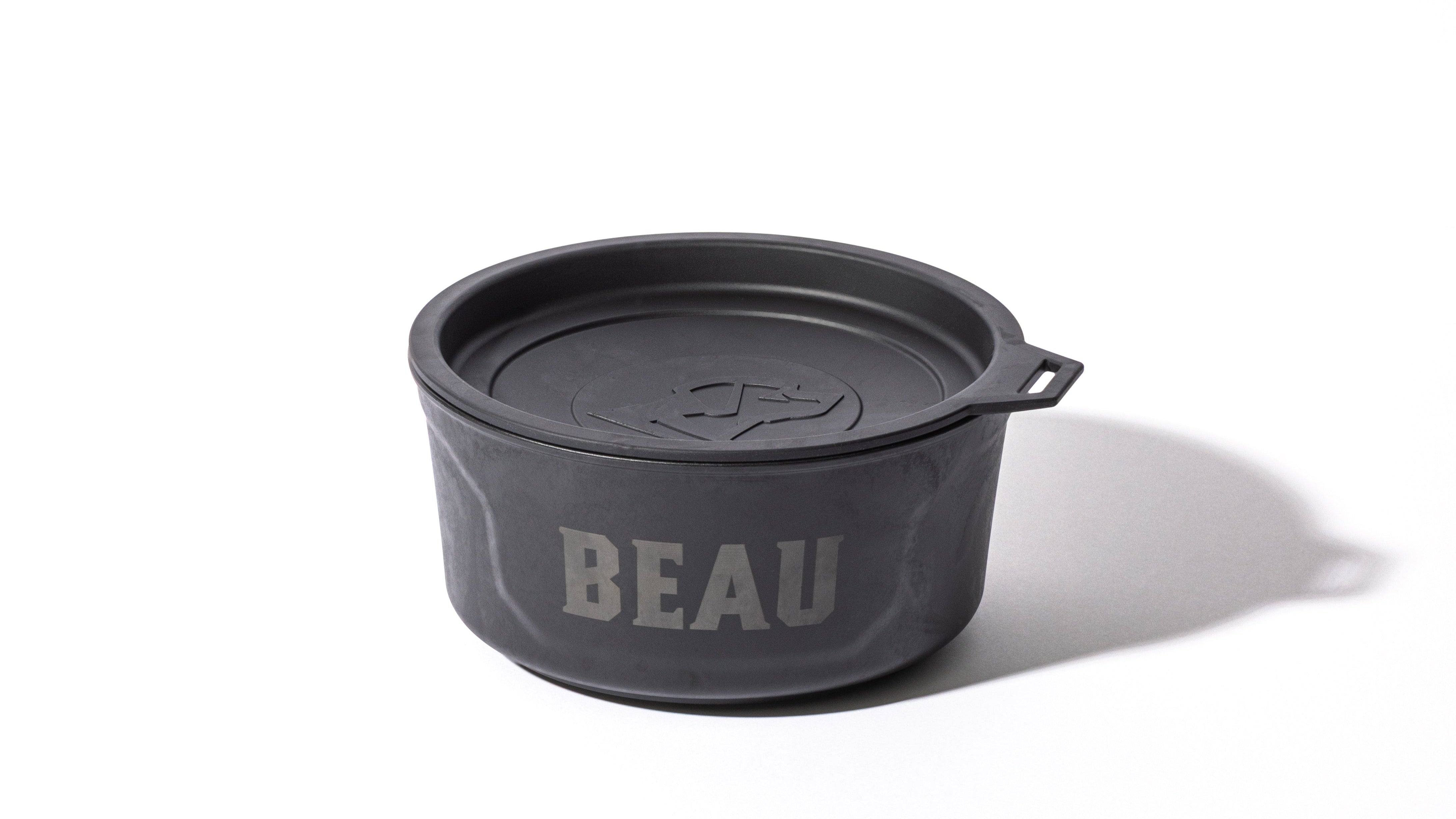 A black, round container with a fitted lid, featuring the word BEAU in bold white letters on the front, placed on a white surface with a subtle shadow—perfect for storing treats for your loyal working dog by the crate.