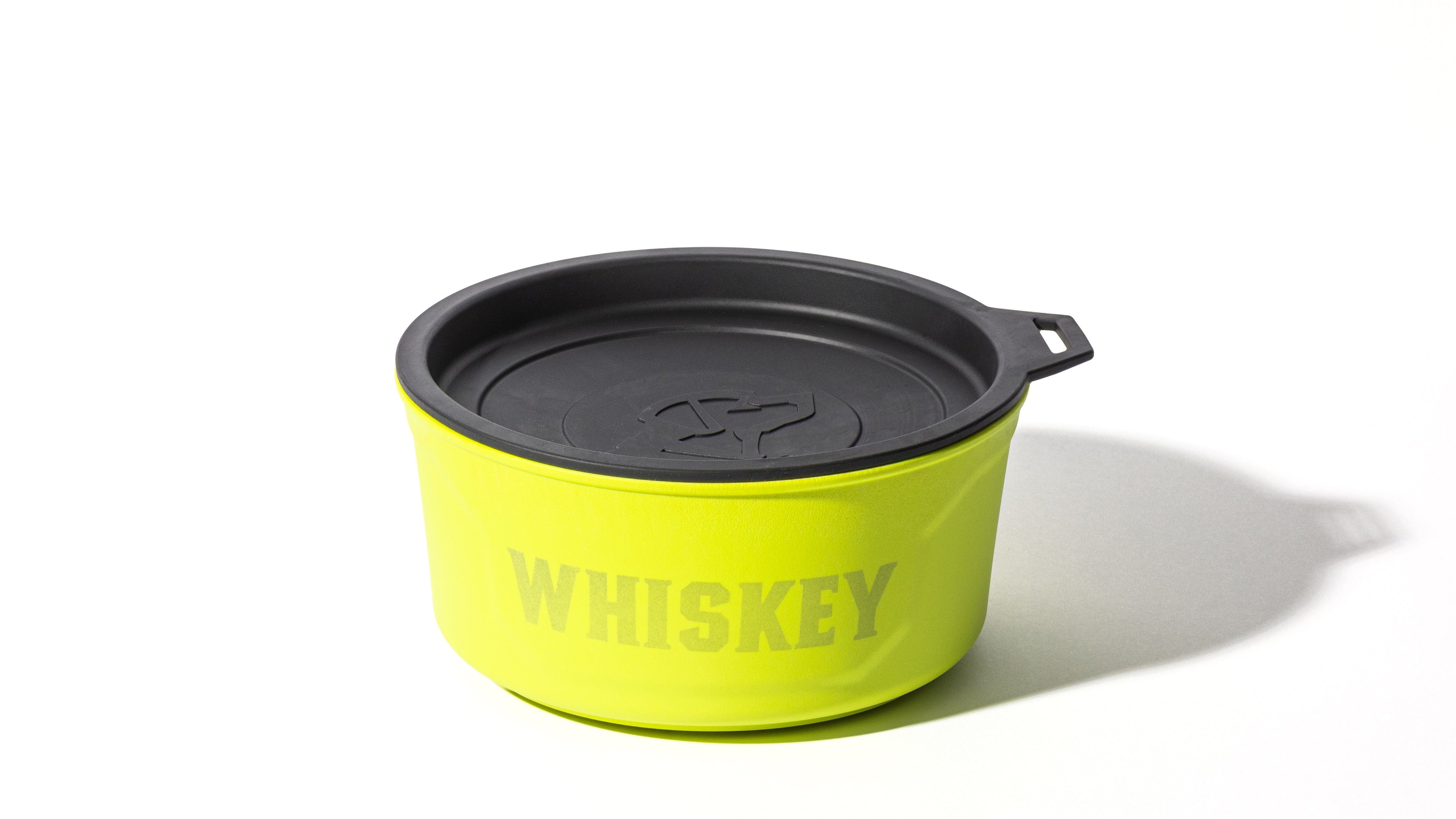 A round, bright yellow container with a black lid and the word WHISKEY printed on the side, photographed against a white background with a shadow to the right—perfect for storing treats in a working dog kennel.