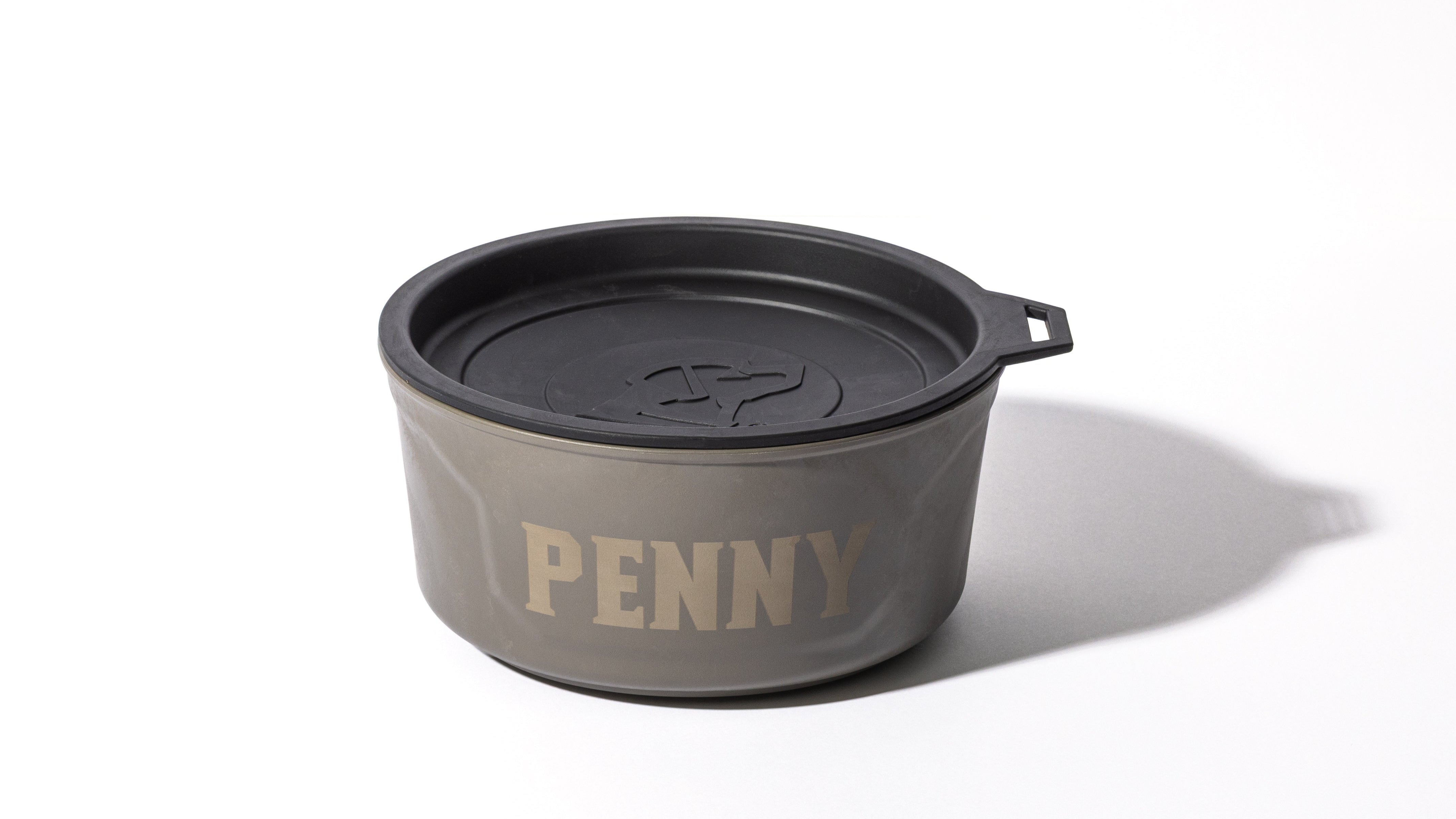 A gray bowl with a black lid, featuring the name PENNY printed in large letters on the side—perfect outdoor gear for your hunting dog. The lid has a circular pattern, a small handle tab, and the bowl casts a shadow on a white background.