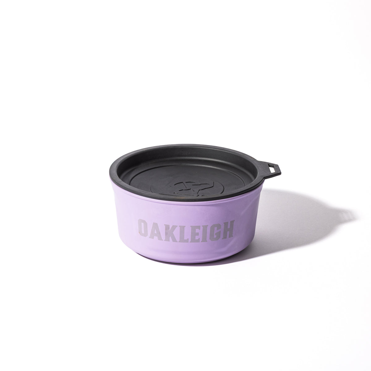 The GUNNER DOG BOWL - LAVENDER, a limited-edition bowl from GUNNER’s Color Fetch collection, features a black lid, small handle, and OAKLEIGH in bold gray letters on the front. It sits on a white background with shadow to the right.