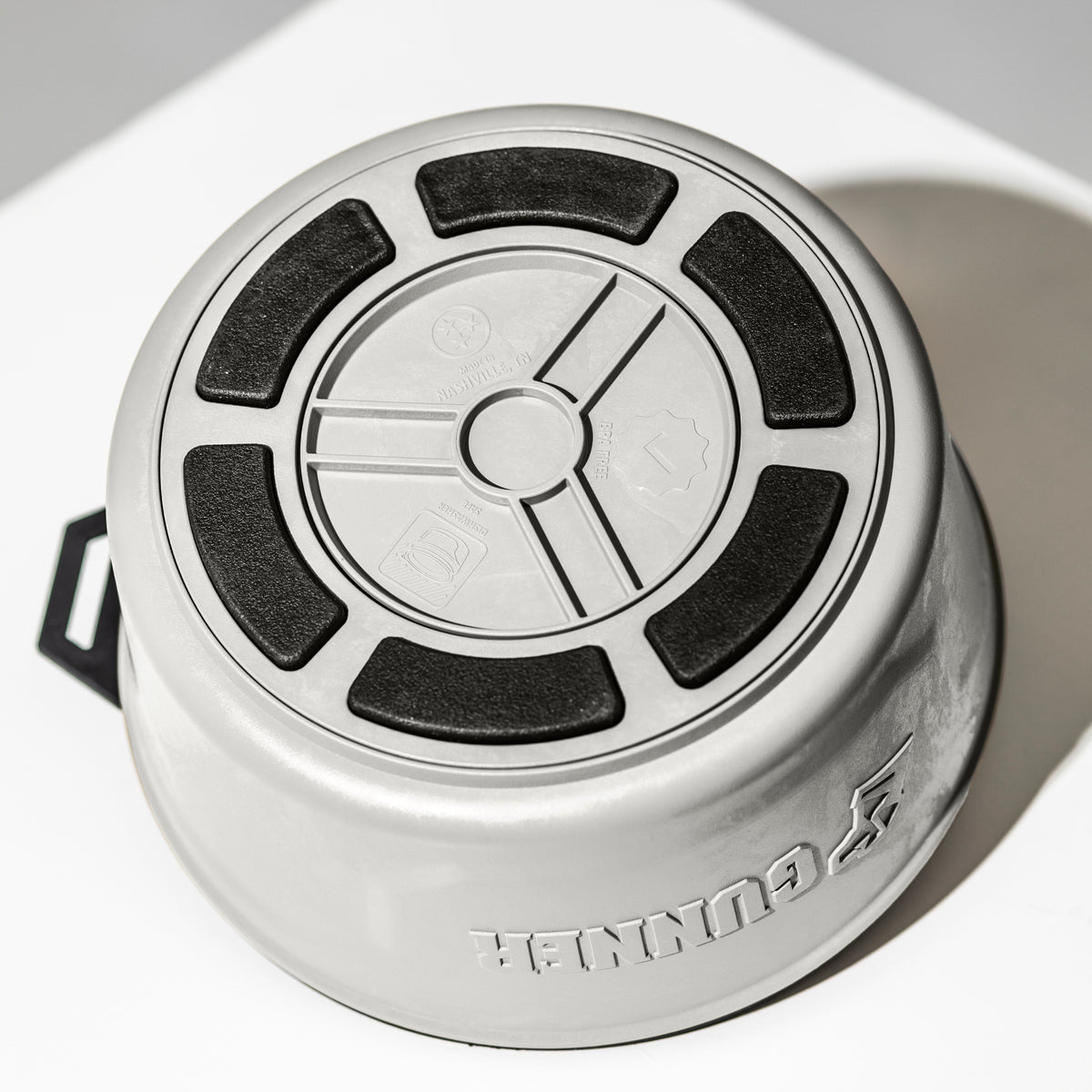 A gray GUNNER DOG BOWL - GUNNER YARD by GUNNER, made in America, is pictured upside down on a white surface, highlighting the black non-slip rubber grips and the patterned bottom design.