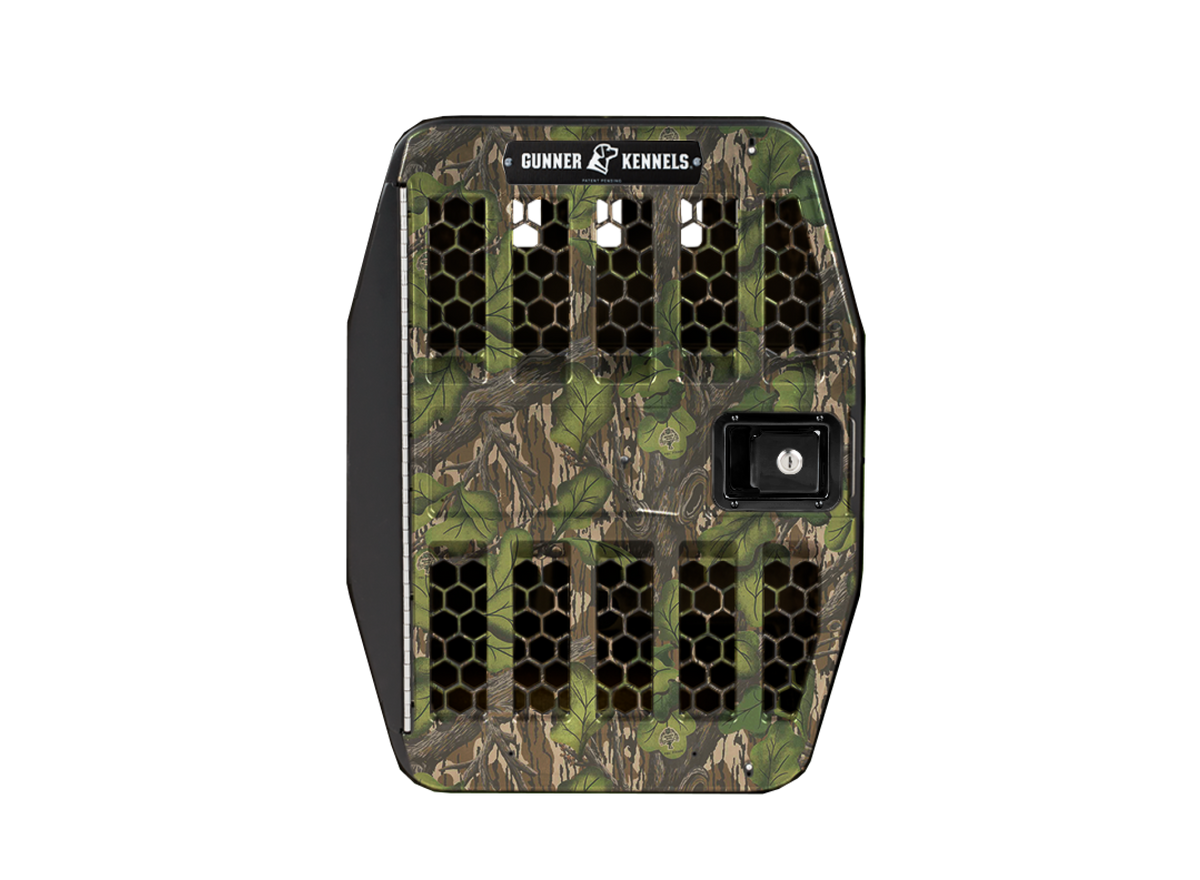 The GUNNER G1™ Kennel Door in Mossy Oak Full Foliage features black ventilation grilles, a locking latch, and branded detailing. Shown on a white background, it’s designed for easy compatibility as a replacement door.
