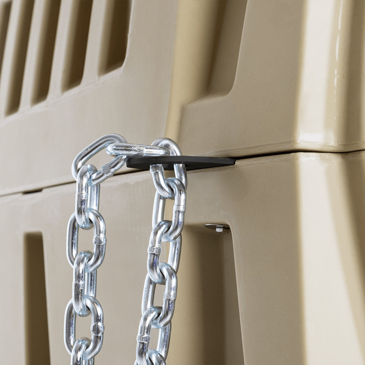 A close-up of a thick metal chain from the SECURITY LOCK KIT secured through a slot in two stacked beige plastic crates and looped through a black metal plate, demonstrating added dog crate security.