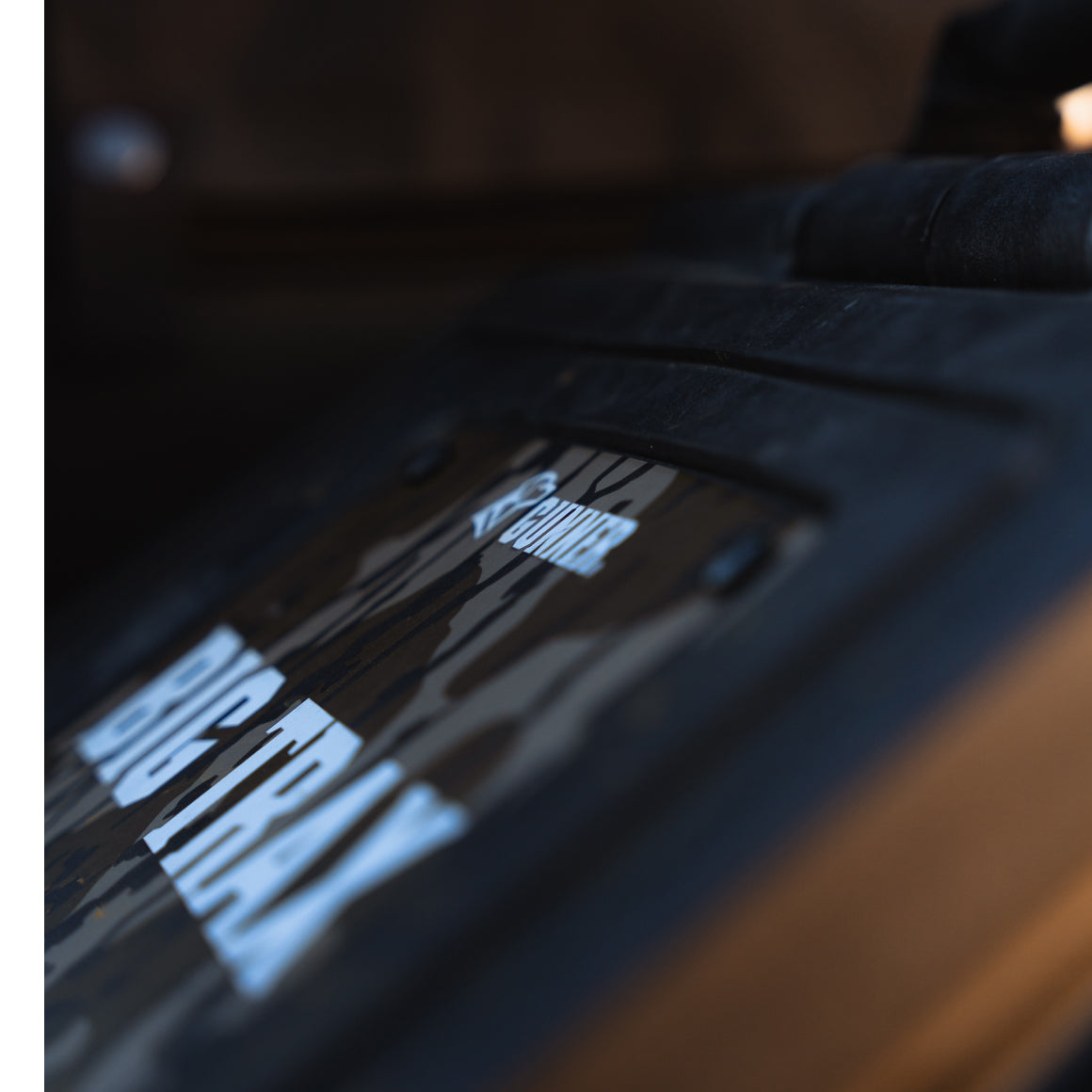 Close-up of a black device with a camouflage-patterned label reading BIG TRAX, partially showing the word SOUNDER above it. Slightly out of focus and shot at an angle, this gear is often used by working dog or hunting dog handlers.