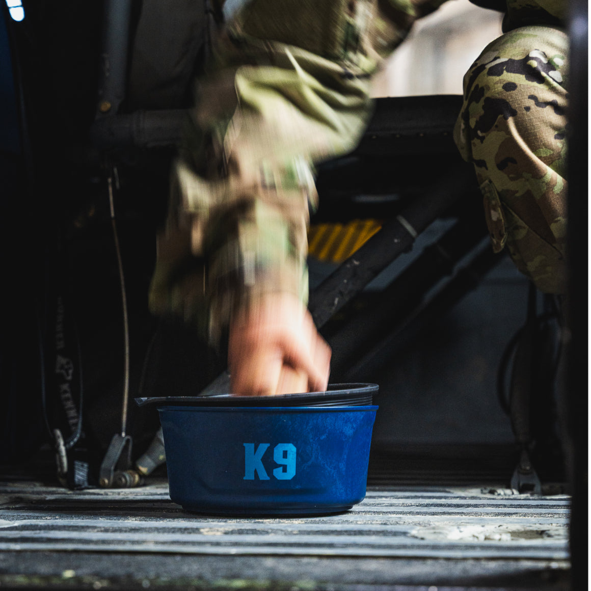 A person in a Navy camouflage uniform reaches for the GUNNER DOG BOWL - NAVY by GUNNER, highlighting the dedication and care that goes into every limited-edition Color Fetch accessory.