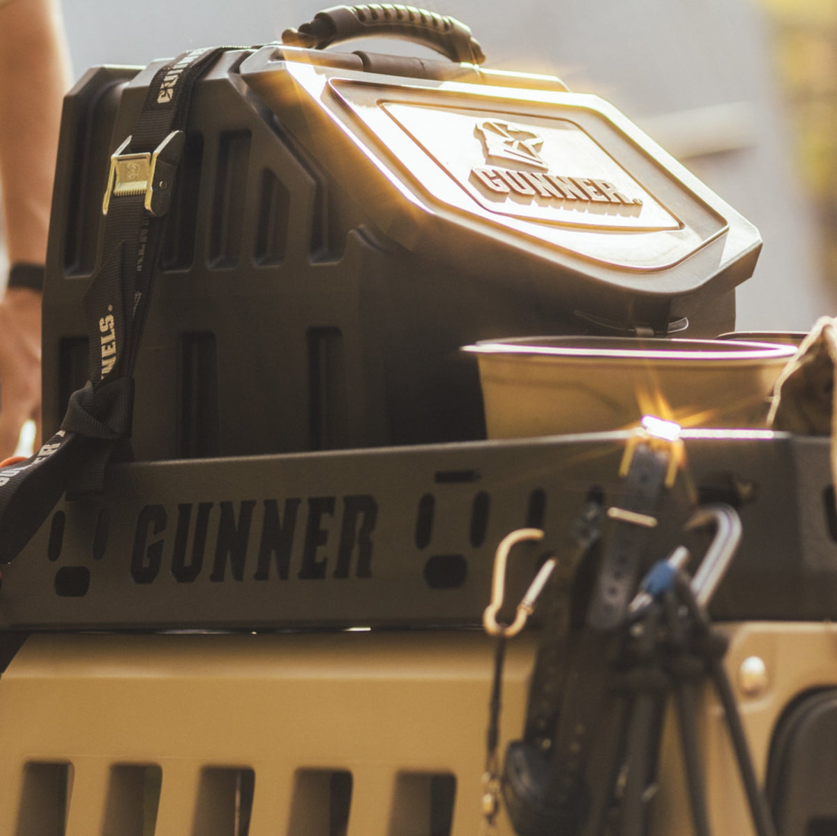 Close-up of the GUNNER Kennel Rack BLACK, a sturdy black and tan pet crate seamlessly integrated into a truck bed kennel storage system; handle, bowl, dog leash, and keys are attached, all bathed in warm sunlight.