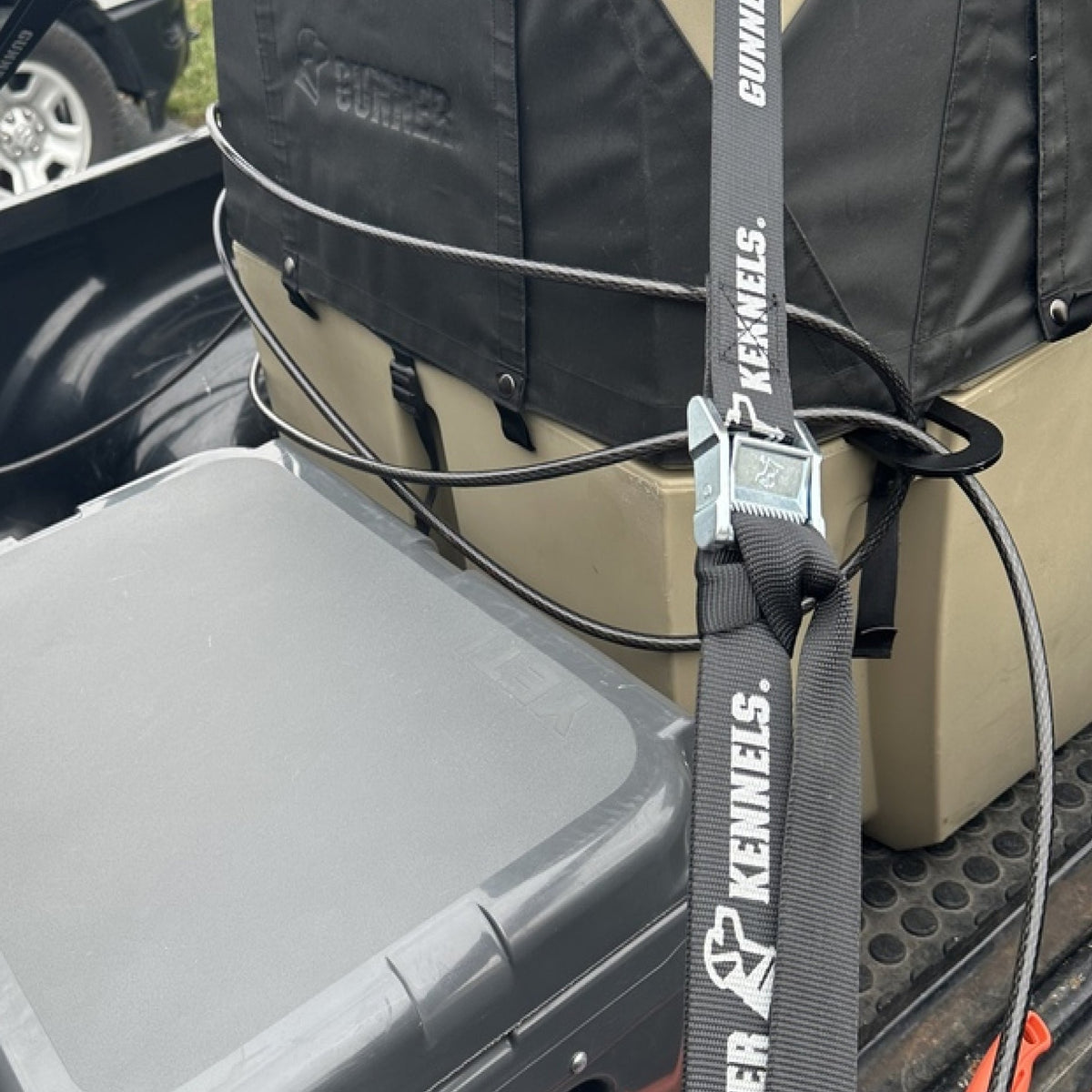 A close-up shows a vehicle dog crate secured in a truck bed using the SECURITY LOCK KIT. Next to the crate is a gray storage bin, emphasizing dog crate security with the SECURITY LOCK KIT in an outdoor setting.