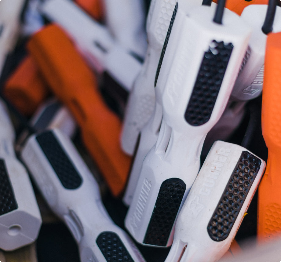 A close-up of several white and orange screwdriver handles piled together, showing textured black grips and a brand logo, sits beside a sturdy hunting dog kennel in the workshop.