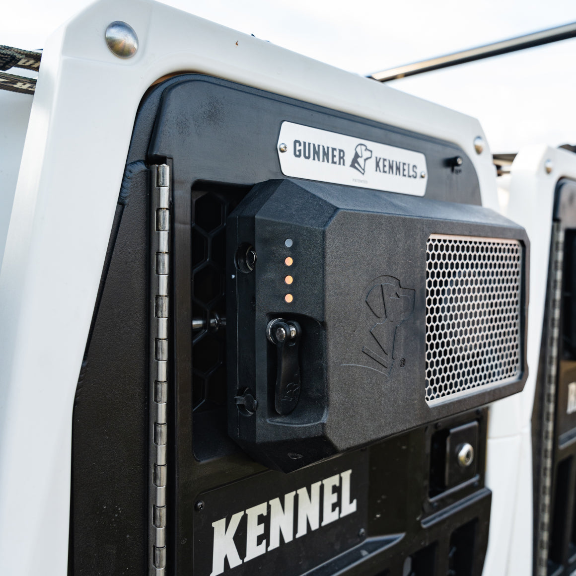 Close-up of a black and white Gunner dog crate door, featuring a secure latch with four orange indicator lights and a metal mesh ventilation panel—essential outdoor gear for your hunting dog. The word KENNEL is printed below the locking mechanism.