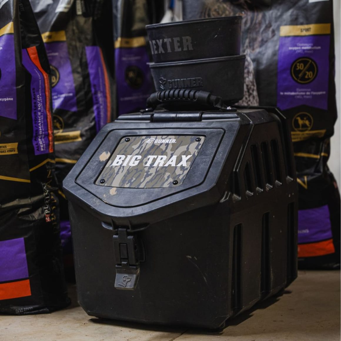 A sturdy black GUNNER FOOD CRATE by GUNNER sits on the floor amid large dog food bags. A personalized black bowl and a travel bowl are stacked on top of the container.