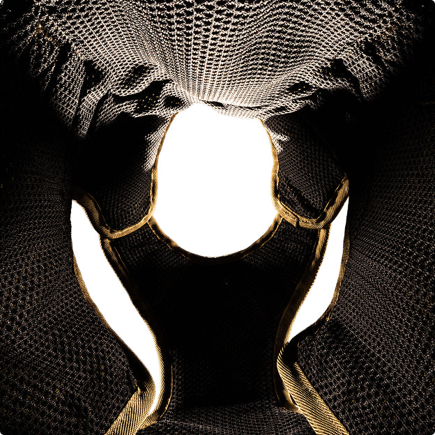 A close-up, abstract image of a textured, dark mesh fabric with gold edges forming a symmetrical pattern around a central white, oval-shaped empty space—reminiscent of the sturdy materials found in premium outdoor gear for working dogs.