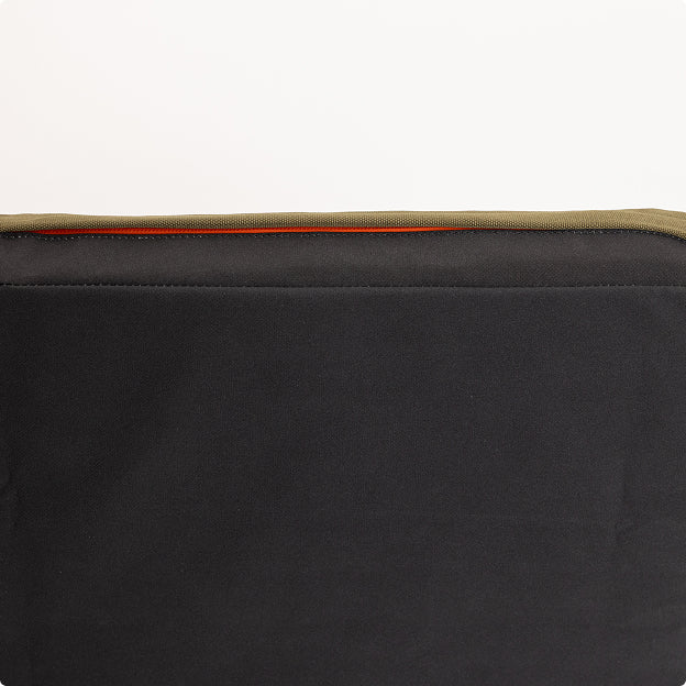A close-up of a black fabric item with a khaki green edge and a small section of orange trim, against a plain white background—perfect for outdoor gear such as a hunting dog kennel.