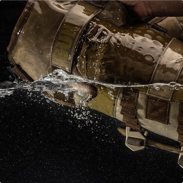 A close-up of a brown tactical bag or vest, partially submerged in water near a dog kennel, with bubbles and water droplets visible, highlighting its durable, water-resistant material.