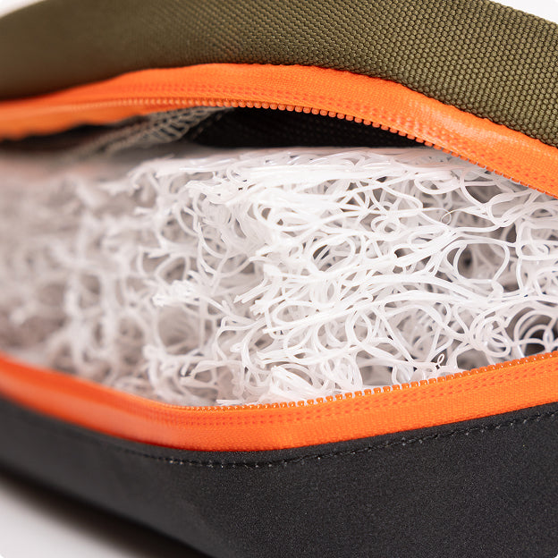 A close-up of a zippered bag partially open, revealing a white, tangled mesh material inside. The zipper is orange, and the bag is made of green and black fabric—evoking the sturdy design often found in dog kennel accessories for hunting dogs.