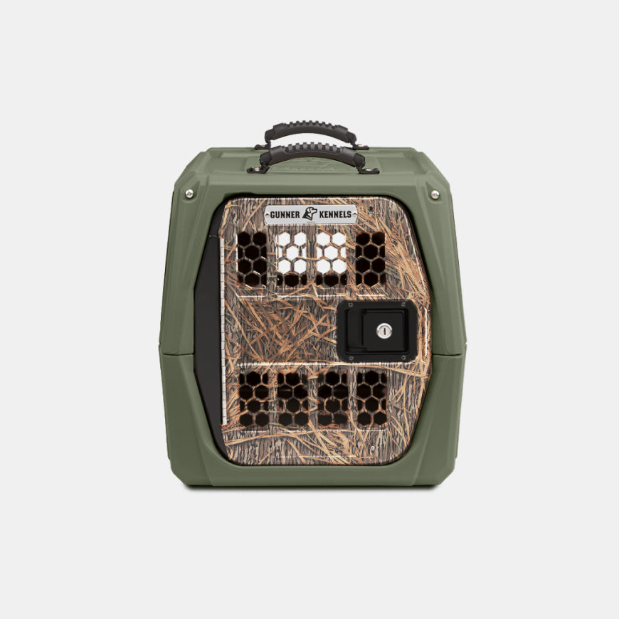 A green dog crate with a camouflage-patterned door, multiple ventilation holes, a black handle on top, and a lockable latch on the front. Perfect for outdoor gear, the door displays the Gunner Kennels brand name.