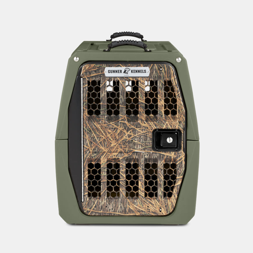 A green pet kennel with a camouflage-patterned, ventilated front door and a secure latch, perfect as an outdoor gear essential for any hunting dog. The label reads Gunner Kennels. The background is plain white.
