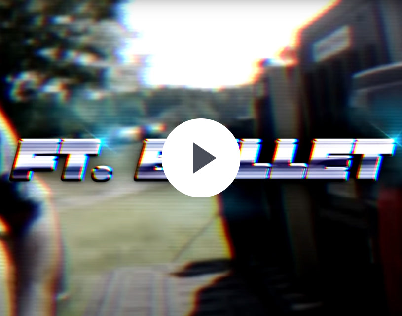 A blurred, glitchy image with bold, distorted text reading FT. BULLET across the center. The background hints at outdoor gear scattered on grass and trees. A play button icon overlays the image.