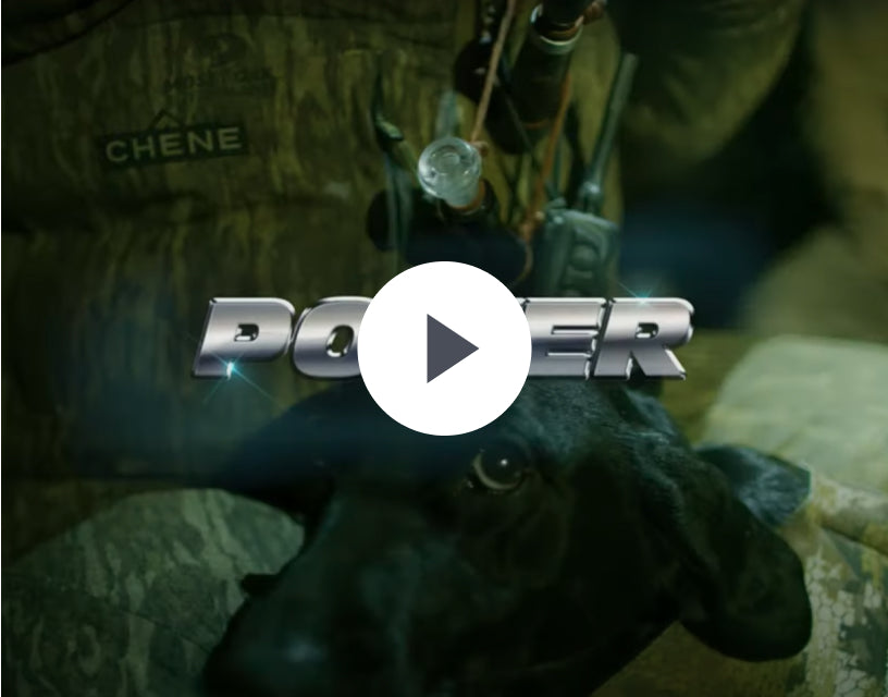 A black working dog with hunting equipment on its back lies next to a person in camouflage clothing labeled CHENE. The word POWER appears in bold metallic letters over the image, highlighting their connection and premium outdoor gear.