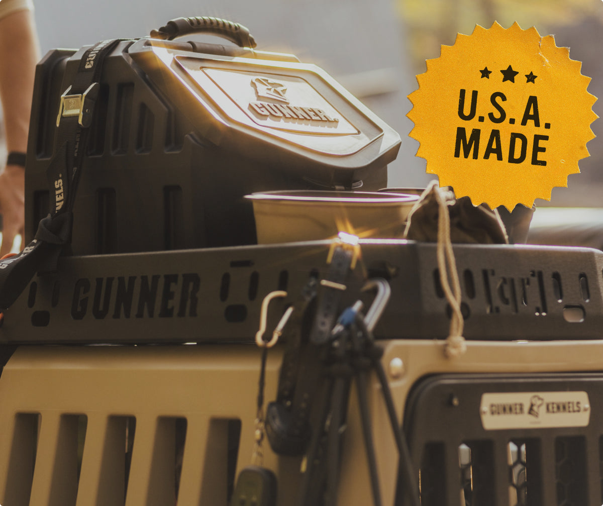 Close-up of stacked GUNNER dog kennels with a dog bowl, various leashes—ideal outdoor gear for any working dog—and a bright orange starburst label reading U.S.A. MADE in the upper right corner.