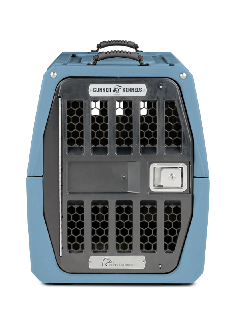 A sturdy blue plastic dog kennel with a metal door, hexagonal ventilation holes, a silver handle on top, and labels reading Gunner Kennels and Ducks Unlimited—ideal for keeping your working dog safe and secure.