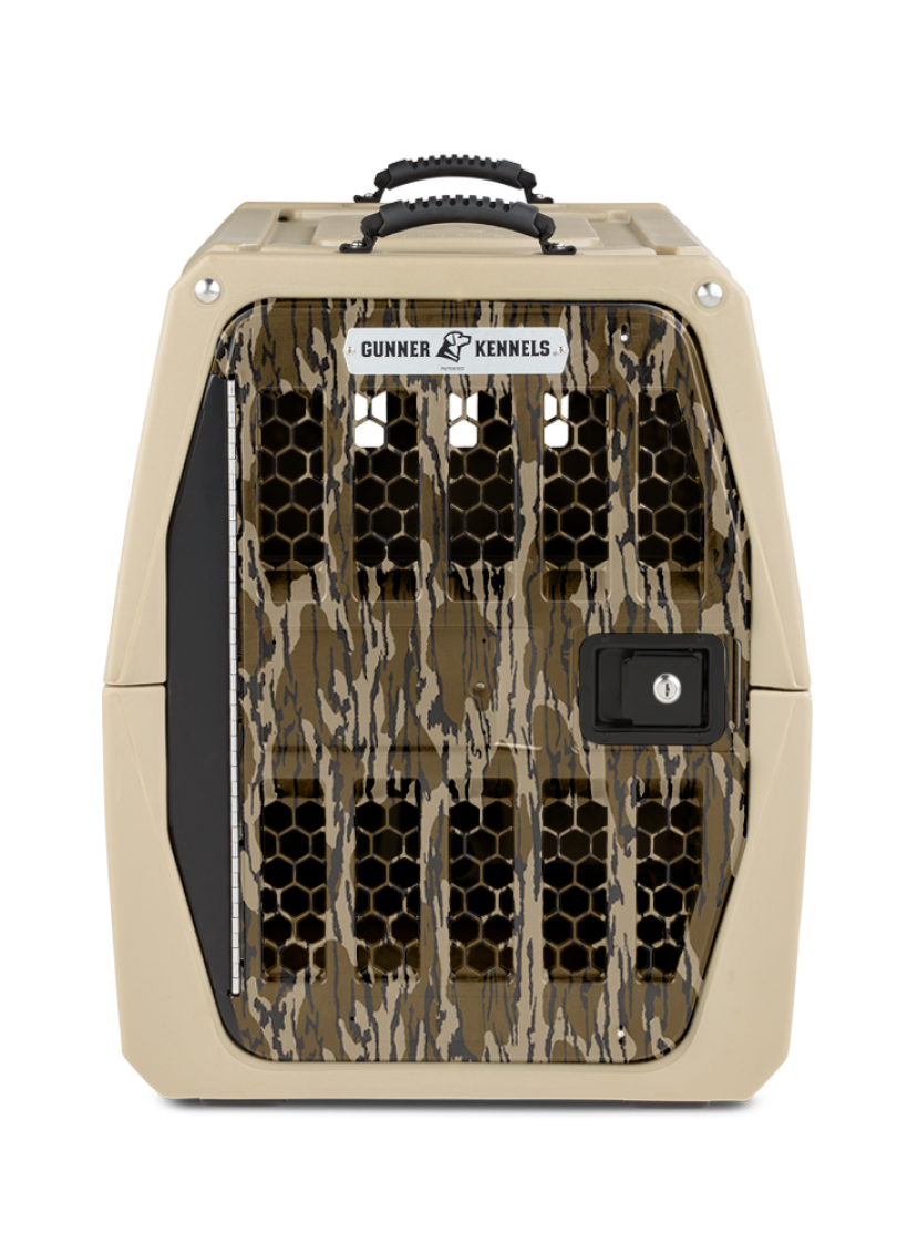 A tan and camo-patterned dog kennel with a black handle on top, hexagonal ventilation holes, and a secure lockable door; labeled “Gunner Kennels” above the door—perfect for keeping your hunting dog safe and comfortable.