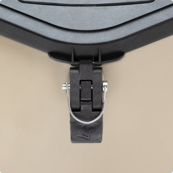 Close-up of a black latch with a metal wire on a beige hard-sided cooler, designed tough enough for any hunting dog. The rubber latch has a small bear icon embossed near the bottom.