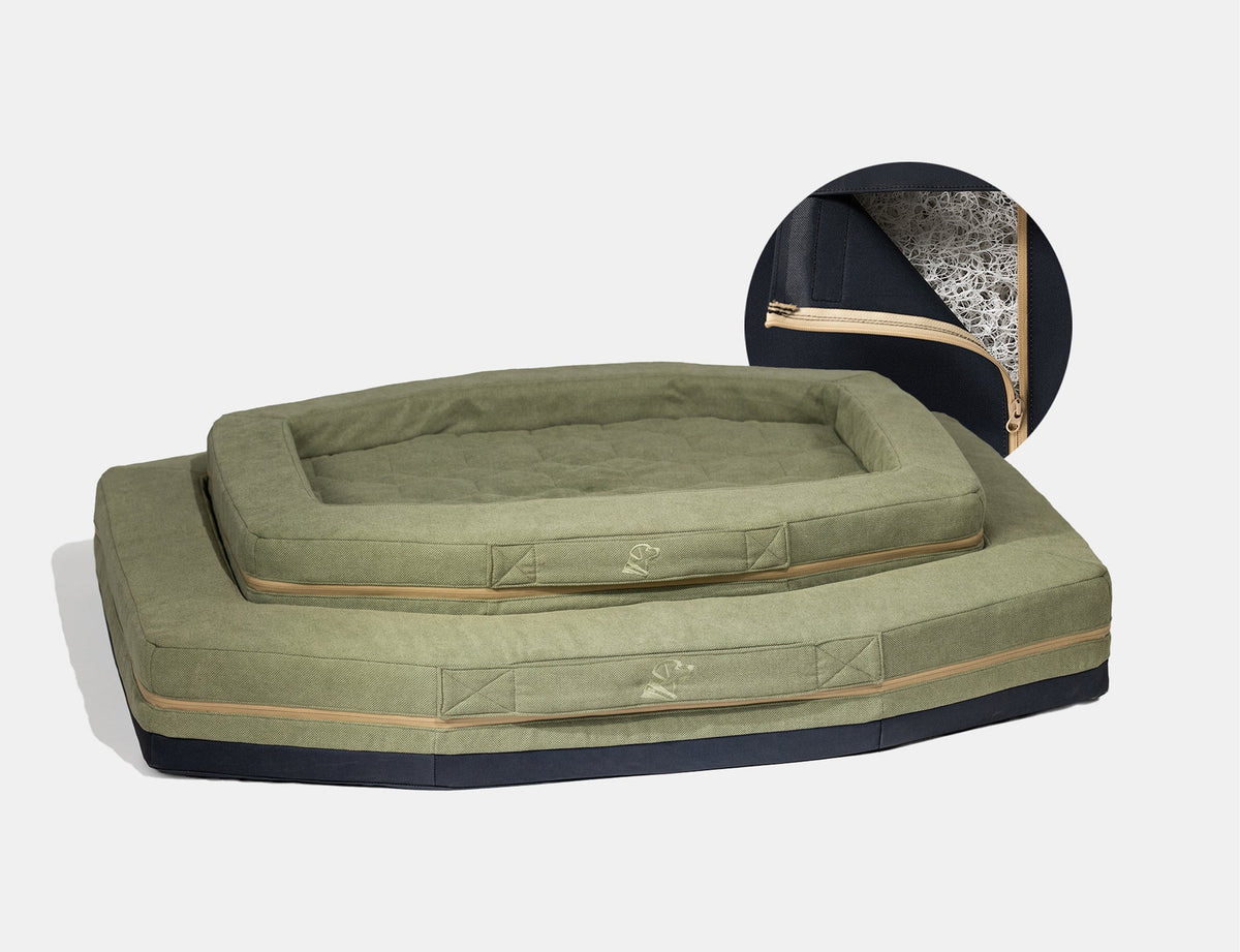 Two olive green rectangular pet beds with raised edges and tan zippers, stacked on top of each other—perfect for a dog kennel or working dog. An inset shows a close-up of the bed’s interior filling through an open zipper.