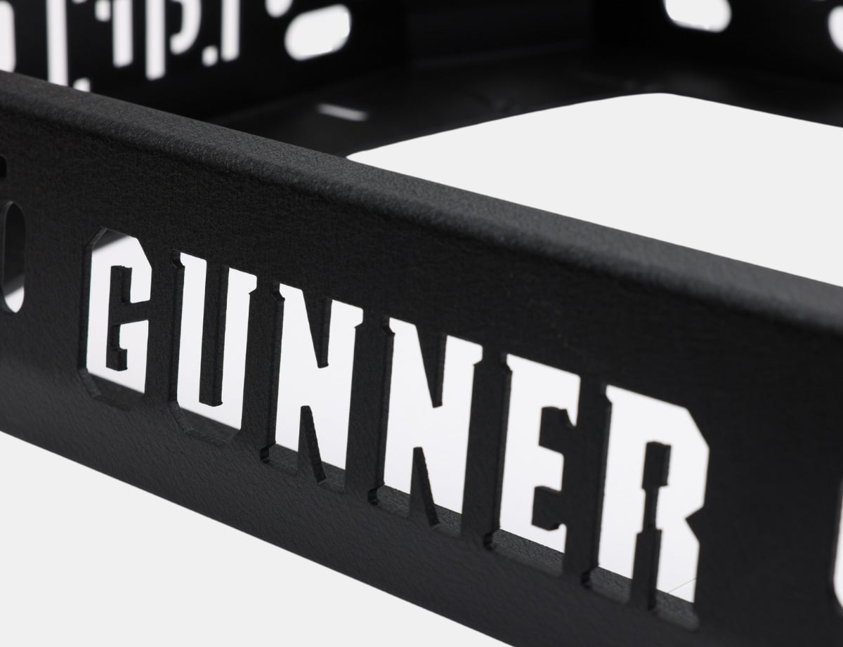 Close-up of a black metal surface with the word GUNNER cut out in bold, capital letters, allowing light to pass through—perfect for showcasing rugged outdoor gear or trusted by any hunting dog kennel.
