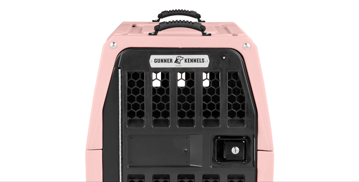 A pink and black Gunner Kennels dog crate is shown from the front, featuring a sturdy metal door, ventilation holes, and two carrying handles on top—perfect for keeping your working dog secure.