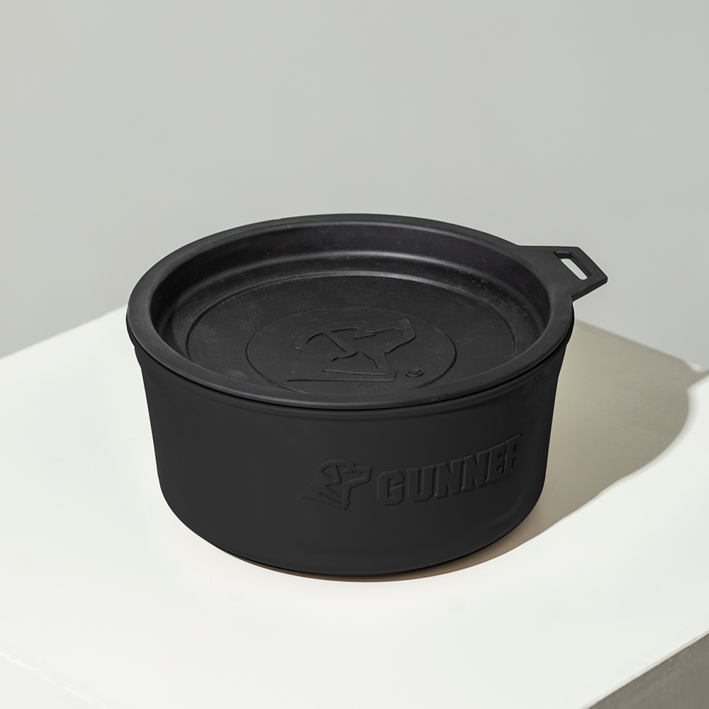 The GUNNER DOG BOWL - BLACK, a round silicone travel bowl with lid, handle, and GUNNER logo, sits on a white surface against a light gray background.