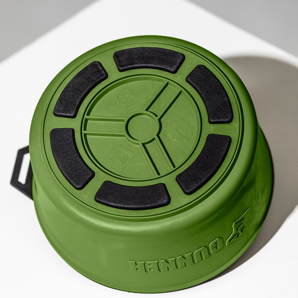 The GUNNER DOG BOWL - DUCK GREEN by GUNNER is a round plastic dog bowl shown upside down, displaying its black textured non-slip base and embossed branding on a white surface.