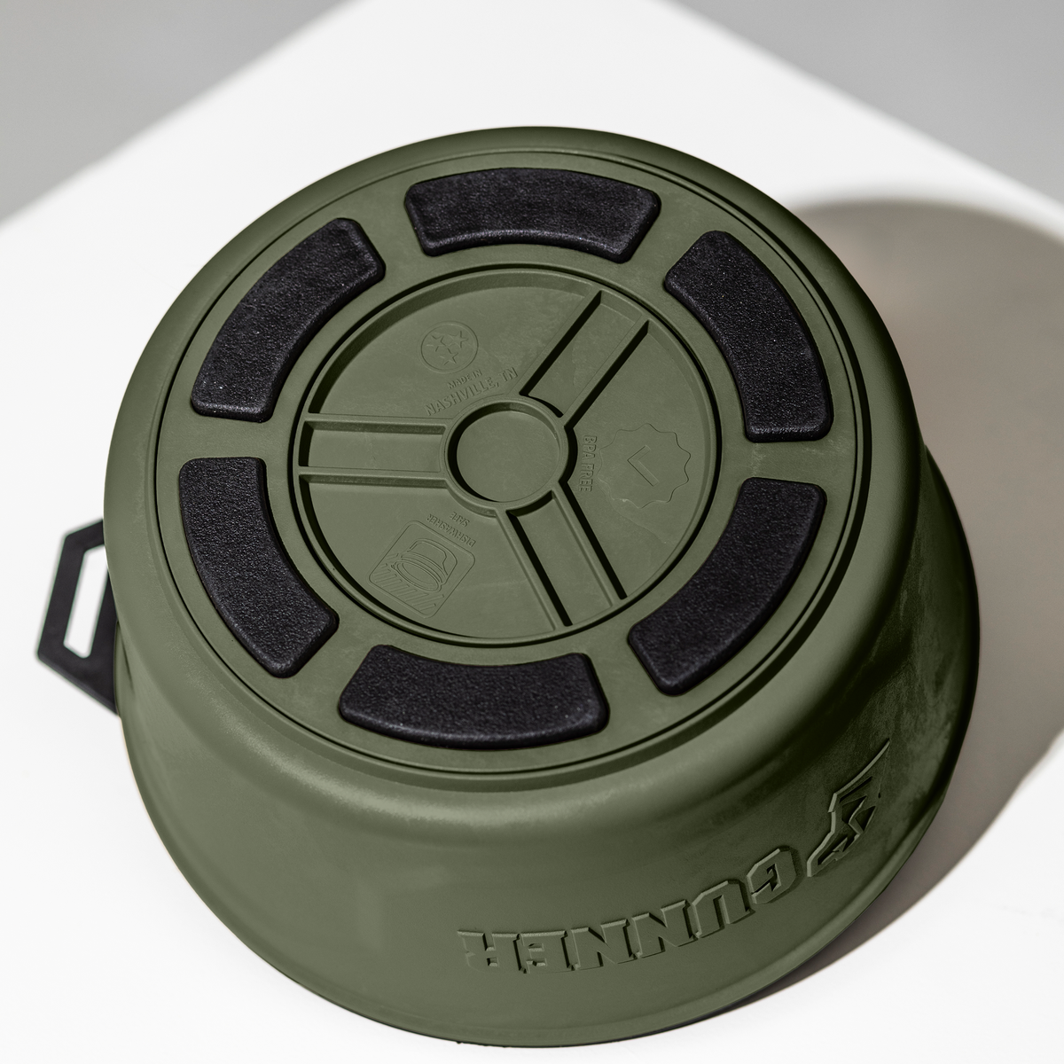 An upside-down GUNNER DOG BOWL - GUNNER GREEN by GUNNER, featuring black non-slip pads and molded symbols on the bottom, is set on a white surface.