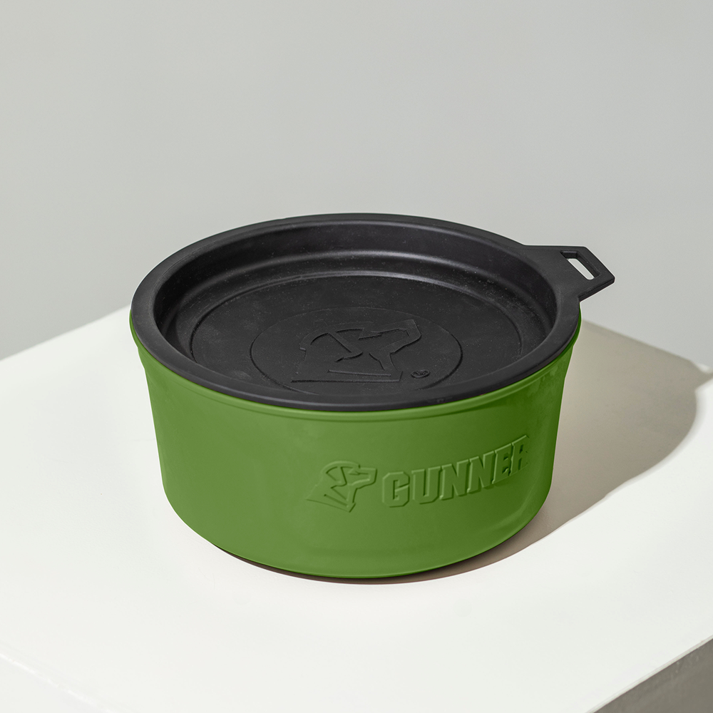 The GUNNER DOG BOWL - DUCK GREEN by GUNNER is a round, portable dog bowl in green and black with a lid and the GUNNER logo embossed on the side and top, shown on a white surface against a light gray background.