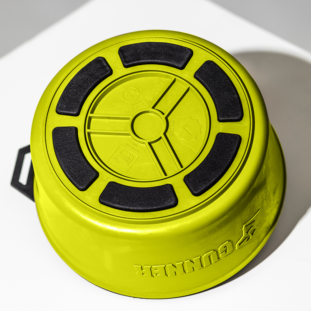 A bright green GUNNER DOG BOWL - SULPHUR SPRINGS is upside down on a white surface, showing black non-slip pads and embossed base symbols. The GUNNER brand name is visible on the side.