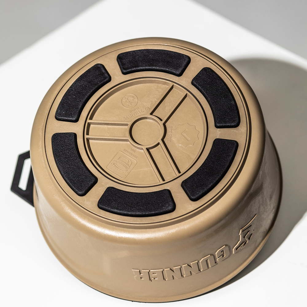 The GUNNER DOG BOWL - TAN by GUNNER is shown upside down on a white surface, featuring black non-slip pads, embossed icons on the bottom, and the word GUNNER visible on the side.