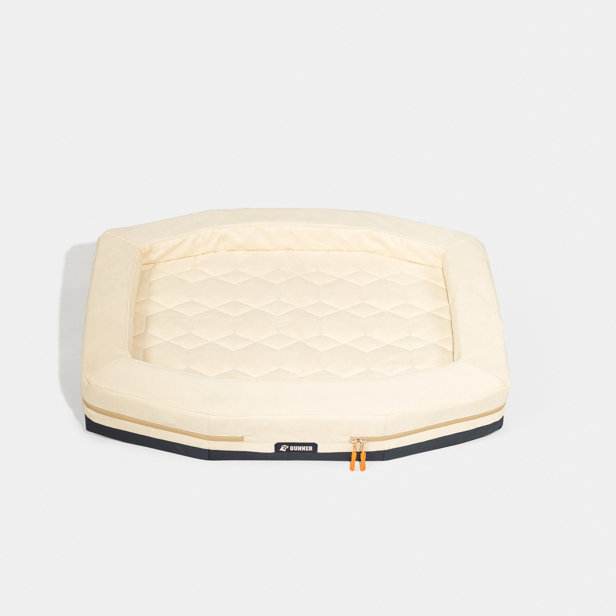 The GUNNER HOMESTEAD DOG BED Oak is a rectangular, beige pet bed with a quilted center, raised edges, black trim, and orange zipper pulls. Durable and easy to clean, its shown on a white background.