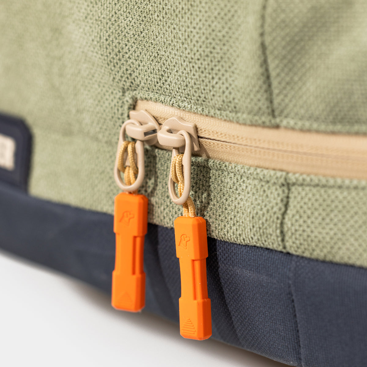 Close-up of the GUNNER HOMESTEAD DOG BED in Treeline Green, featuring a beige zipper with two durable orange plastic pulls, each marked with a small logo.