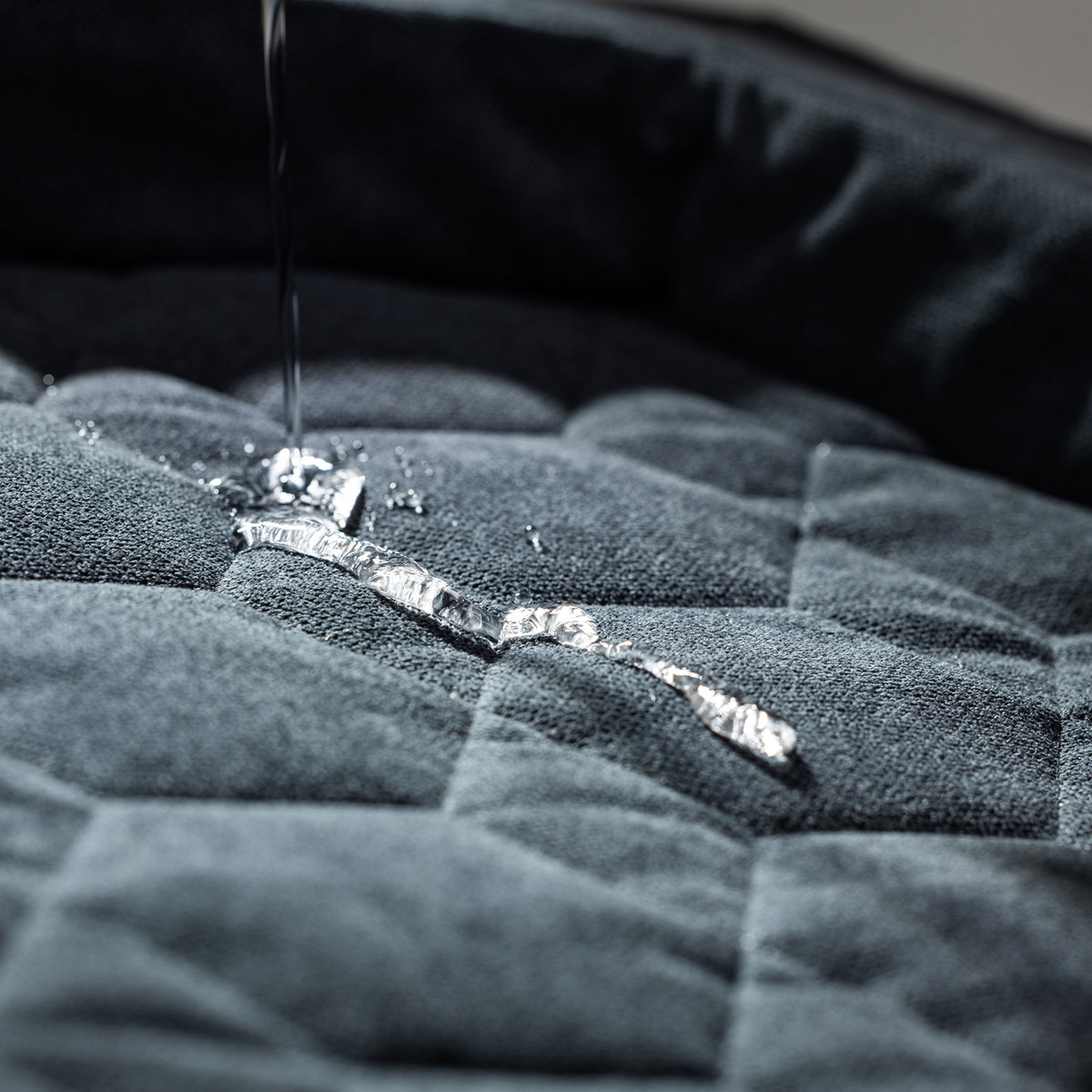 Close-up of water on the GUNNER HOMESTEAD DOG BED Harbor Blue shows liquid beading up on the quilted surface, demonstrating its durable, easy-to-clean, and water-resistant design.